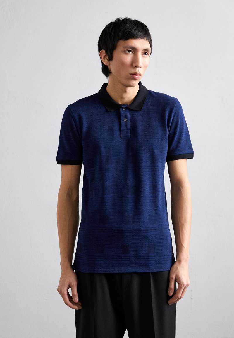 Marinblå polo skjorta med en texturerad tyg, svart krage och muddar, med en tre-knapp placket och en slim fit design.