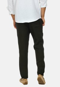 Pantaloni in lino neri con una vestibilità slim, caratterizzati da una parte anteriore piatta e tasche posteriori, indossati con una camicia bianca a maniche lunghe e scarpe color cammello.