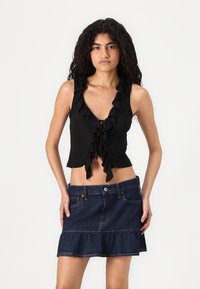 Crop top noir à volants avec un décolleté en V et un laçage à l'avant, associé à une mini-jupe en denim avec un ourlet à volants en plusieurs niveaux et des poches avant.