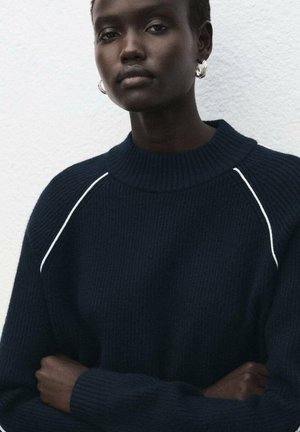 Suéter de punto azul marino con cuello alto y textura acanalada, con costuras blancas decorativas a lo largo de los hombros. Botones no visibles.