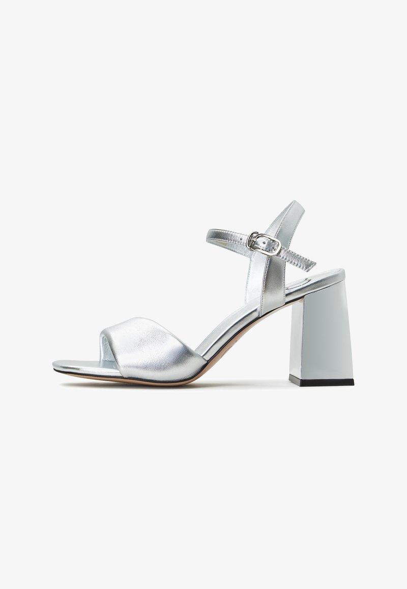 Srebrne sandały na obcasie z odkrytymi palcami i szerokim paskiem; posiadają prostokątny obcas z błyszczącym wykończeniem oraz regulowany pasek wokół kostki.