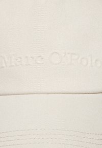 Casquette en coton blanc avec une surface texturée, présentant un logo en relief "Marc O'Polo" à l'avant. Le design est simple avec une visière courbée.