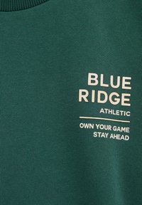 Zeleno atletsko sweatshirt iz teksturirane tkanine. Ima belo natisnjen napis: "BLUE RIDGE", "ATHLETIC", "OWN YOUR GAME", "STAY AHEAD".
