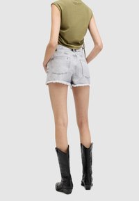 Shorts de denim con dobladillo deshilachado, lavado claro y dos bolsillos traseros. Combinados con una blusa ajustada de color verde oliva y botas cowboy negras hasta la rodilla.