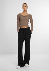 Pruun soonikkidega pikkade varrukatega crop-top, millel on laineline kaelus ja "KANI" logo, koos mustade laia säärega pükste ja valgete tennistega.