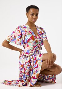 Vestido envolvente colorido con mangas cortas y vaporosas, que presenta un patrón floral en rojo, rosa, azul y verde sobre un fondo beige.