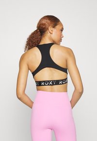 Černá sportovní podprsenka s designem na zadní straně, se zdobným logem. Doplněná vysokými růžovými legínami, hladký materiál, elegantní střih.