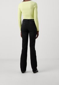 Top de manga larga acanalado en un brillante verde lima, combinado con jeans de campana negros de talle alto. Textura suave con bolsillos estándar y costuras sutiles.