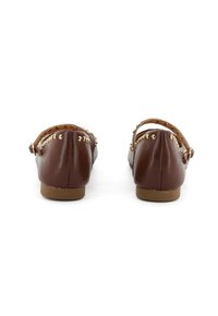 Ballerine in pelle marrone con borchie dorate lungo la fascia e tacco basso. La parte posteriore presenta una forma arrotondata e cinghie alla caviglia per il supporto.