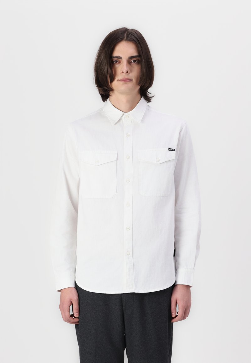 Witte lange mouwen shirt met een button-down kraag, twee borstzakken en een labeldetail aan de linkerkant. De stof lijkt textuur te hebben en is lichtgewicht.