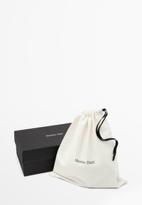 Cotton drawstring bag in off-white with black cord; black rectangular box with white text reading “Massimo Dutti” on both items.