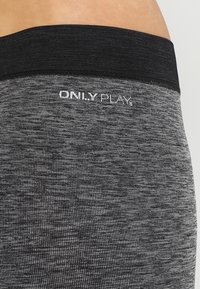 Szare legginsy sportowe z teksturowanym, marmurkowym wzorem; szeroki czarny elastyczny pas; z nazwą marki "ONLY PLAY" w kolorze białym.