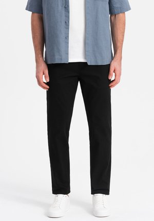 Schwarze Baumwollhose mit geradem Schnitt, kombiniert mit einem hellblauen Kurzarmhemd und weißen Sneakers.