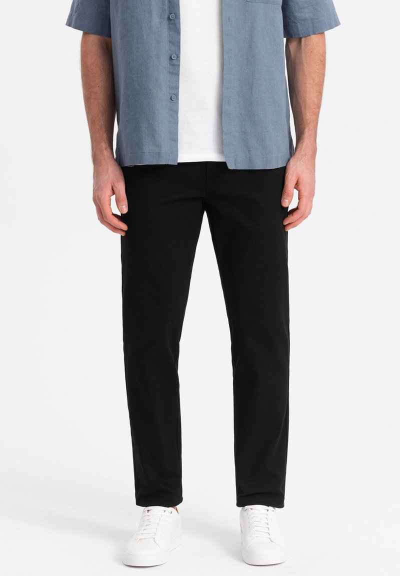 Pantalon en coton noir avec une coupe droite, associé à une chemise à manches courtes bleu clair à boutons et des baskets blanches.