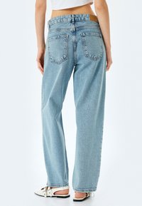 Jeans en denim bleu clair, taille haute, avec une coupe ample. Comprend deux poches arrière et une étiquette en cuir au niveau de la taille. Texture lisse.