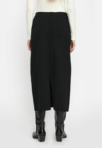 Zwarte gebreide midi-rok met een split aan de achterkant, een zachte textuur en een rechte silhoutte. Gecombineerd met zwarte laarzen met hoge hakken tot de knie.