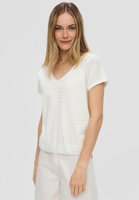 Witte top met korte mouwen en V-hals, gekenmerkt door textuur in horizontale strepen en een relaxte pasvorm, gecombineerd met lichtgekleurde broek.