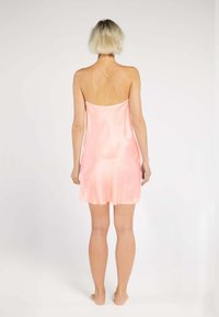 Silky pink nightdress with thin, crisscross straps, a straight cut, and a smooth, flowing texture. Minimalist design, knee-length.