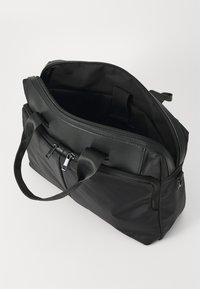 Sort duffel taske lavet af glat syntetisk materiale, med en lynlåslukket hovedrum, to håndtag og en udvendig lynlåslomme.
