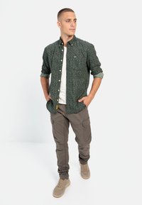 Grønne mønstrede skjorte med knapper, hvid t-shirt under, parret med khaki cargobukser og beige sneakers. Slim fit med oprullede ærmer.