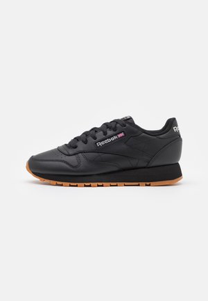 Baskets en cuir noir Reebok avec semelle en gomme, logo latéral et lacets, vues de profil sur fond blanc.