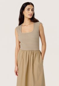Beige ribstrikket top med firkantet udskæring, parret med en lys beige, sammensyning nederdel med lommer. Glat tekstur og tætsiddende design.
