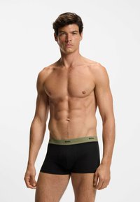Boxer neri con una fascia elastica verde con la scritta "BOSS". Il tessuto sembra morbido con una texture liscia, aderente al corpo.