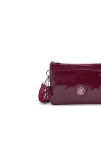 Sac à main bordeaux brillant avec quincaillerie en argent, doté d'un charme en forme d'ours et d'un logo rond. Design compact avec une fermeture éclair et une bandoulière détachable.