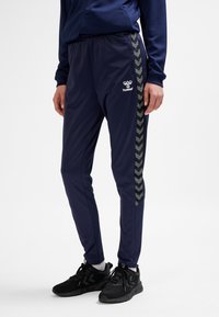 Granatowe spodnie sportowe wykonane z lekkiego materiału z bocznym paskiem w wzór jodełki. Elastyczna talia i haftowane logo z przodu.