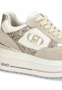 Beige i bijele tenisice s sjajnim akcentima, bež vezicama, debelim potplatom, metalnim logotipom sa strane i tekstom "LIU·JO #HRASTI#JEDINSTVENI#VJEČNI" na srednjem dijelu potplata.