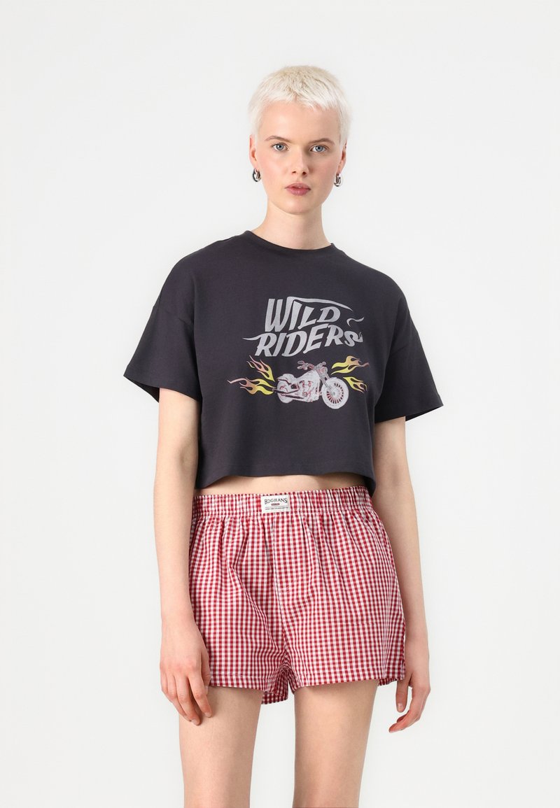 Black cropped t-shirt with "WILD RIDERS" graphic and motorcycle design. Paired with red and white gingham check shorts with an elastic waistband.