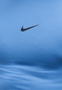 Logo Nike swoosh noir sur un tissu bleu clair lisse, montrant des plis doux et une texture subtile.