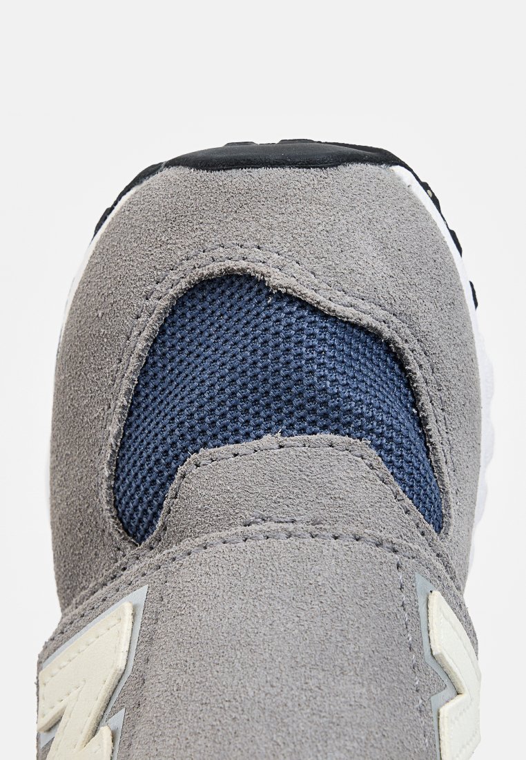Baskets en daim gris avec un panneau en maille bleu marine, tige texturée, accents blancs et semelle extérieure noire. Présente un design contemporain.