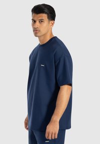T-shirt a maniche corte di colore blu navy con colletto a girocollo, realizzato in misto cotone. Presenta una piccola patch con logo sul petto e una vestibilità comoda.