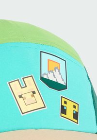 Zielona i turkusowa czapka z trzema naklejkami w stylu pikselowym: jasnobrązowy królik, górski krajobraz z zachodem słońca i żółty blok.