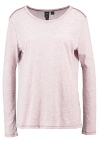 Långärmad, ljusrosa topp i mjukt tyg med rund halsringning och sömnadsdetaljer längs axlarna. Slät textur och avslappnad passform.