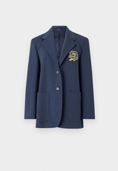 Navy blazer made from textured fabric, featuring a notched collar, two front pockets, and a gold embroidered patch with "1993 Weekend."