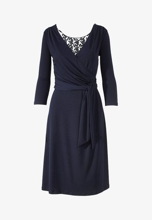 Robe navy à encolure croisée avec des manches trois-quarts, mettant en avant un empiècement en dentelle et une ceinture à la taille, confectionnée en tissu doux et extensible.