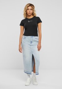 T-shirt noir à manches courtes avec logo blanc, associé à une jupe maxi en denim bleu clair avec fente avant et ourlet effiloché, portée avec des baskets blanches.
