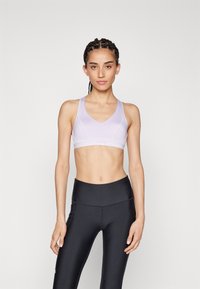Fénylila sportmelltartó V-nyakú kivitelben, rugalmas anyagból, sima textúrával és minimalista stílussal. Fekete, magas derekú leggings.