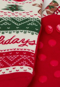 Red and cream socks with festive patterns, including trees and holiday text. One side features raised red dots on a solid red background.