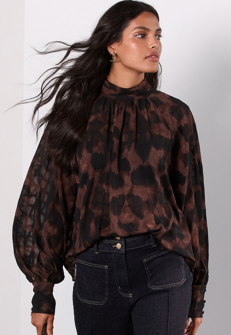 Brown and black printed blouse with a high neckline, pleated design, and long billowy sleeves, made from lightweight fabric.