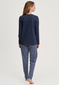 Marineblauw long sleeve top gecombineerd met gestippelde pyjamabroek in marineblauw en wit, met een zachte textuur en een relaxte pasvorm.