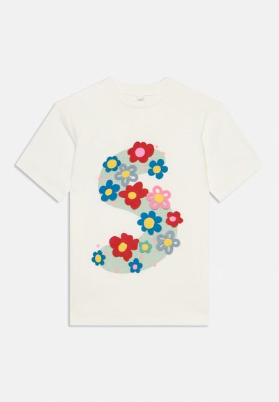 Άσπρο κοντομάνικο T-shirt με ένα μεγάλο, καμπύλο πράσινο σχήμα διακοσμημένο με κόκκινα, μπλε, ροζ και γκρι λουλούδια στο μπροστινό μέρος.