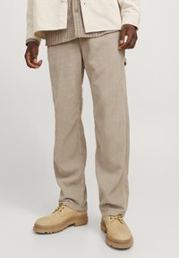 Beige corduroy pants with a straight leg fit, featuring vertical ridges and side pockets, paired with tan lace-up boots.