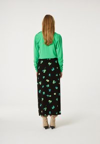 Groene blouse met lange mouwen en pofschouders, gedragen met een zwarte maxi-rok met een bloemenpatroon in turkoois en groene tinten.