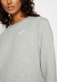 Sweatshirt gris en tissu doux, avec un col rond et un petit logo Nike blanc brodé en haut à gauche.