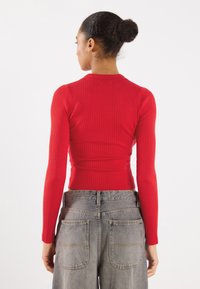Rotes, geripptes Langarmoberteil mit rundem Ausschnitt, kombiniert mit grau-gewaschenen Jeans in hoher Taille mit großen Gesäßtaschen.