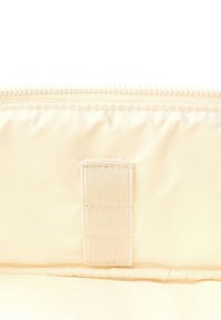 Kremowa torba nylonowa z zamkiem błyskawicznym na górze i rzepem po boku, gładka struktura, minimalistyczny design.