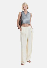 Pruhovaný šedobiely bezrukávový crop top s výstrihom do V, kombinovaný s vysokými, širokými nohavicami v krémovej farbe.